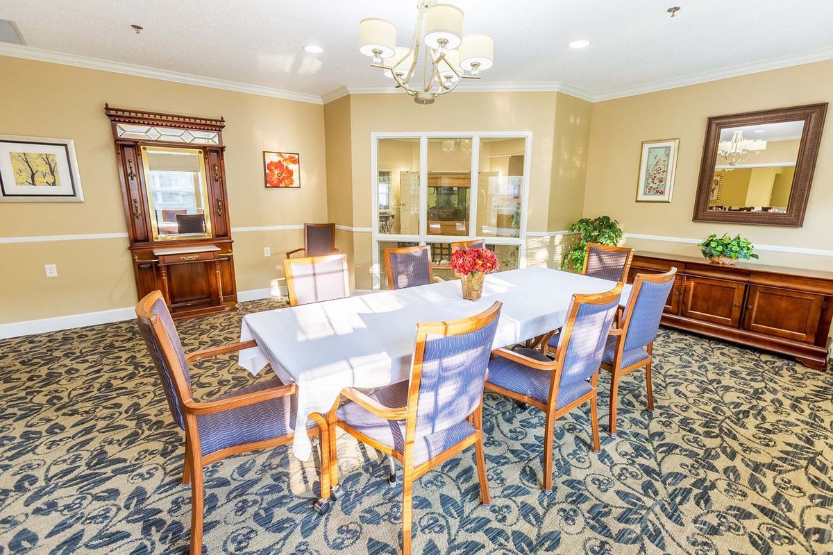 A well-lit dining room with a table and six chairs, featuring elegant decor and a floral carpet.