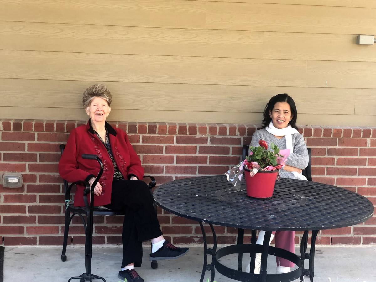Two people sitting at a table outside, with a potted plant on the table.