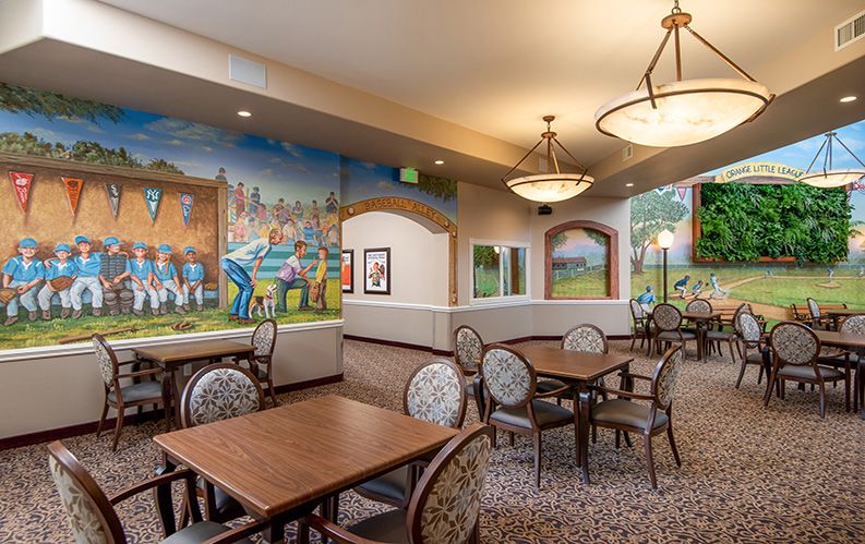 A brightly lit dining area with decorative murals, featuring tables and chairs arranged for a comfortable dining experience.