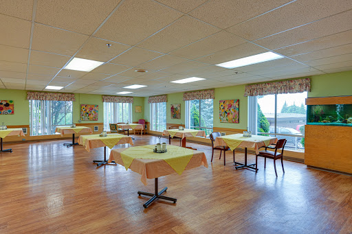 A spacious dining room featuring several tables and chairs, adorned with green walls and artwork, illuminated by natural light from large windows.