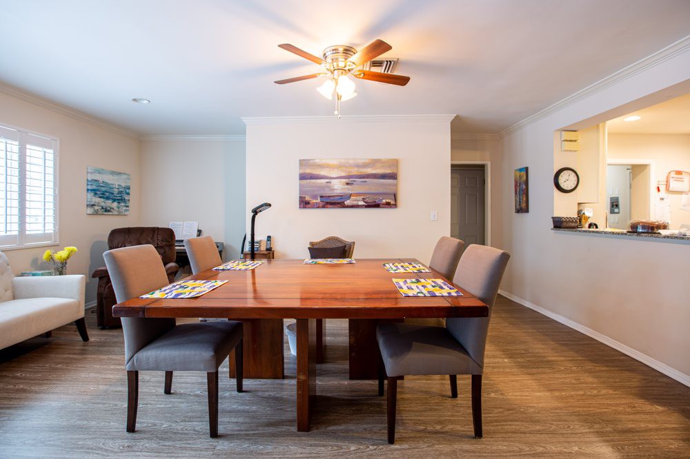 A cozy dining room with a wooden table, upholstered chairs, and a ceiling fan, decorated with wall art and featuring a wooden floor.