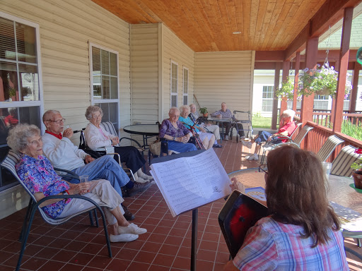 A group of seniors enjoying a musical performance on a sunny porch.