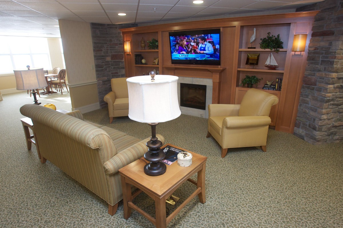 A cozy living room with a TV, sofas, and armchairs arranged around a central wooden table.