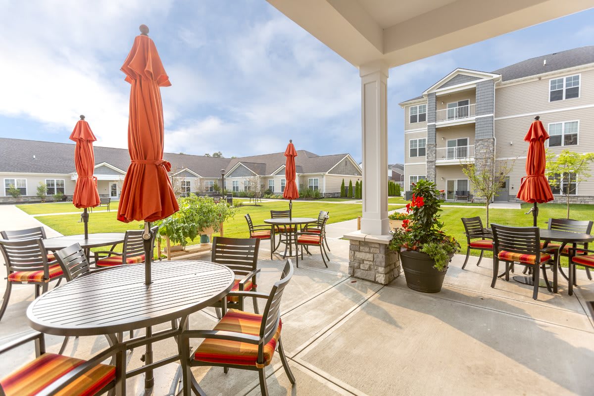 A well-maintained outdoor patio area with tables, chairs, and red umbrellas overlooking landscaped grounds and nearby apartment buildings.