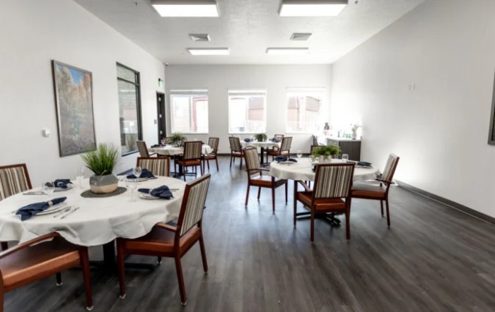 A bright and minimalist dining room with several tables and chairs, adorned with plants and receiving ample natural light.
