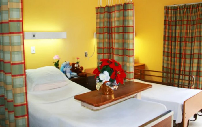 A hospital room with a bed, floral arrangement, and a privacy curtain.