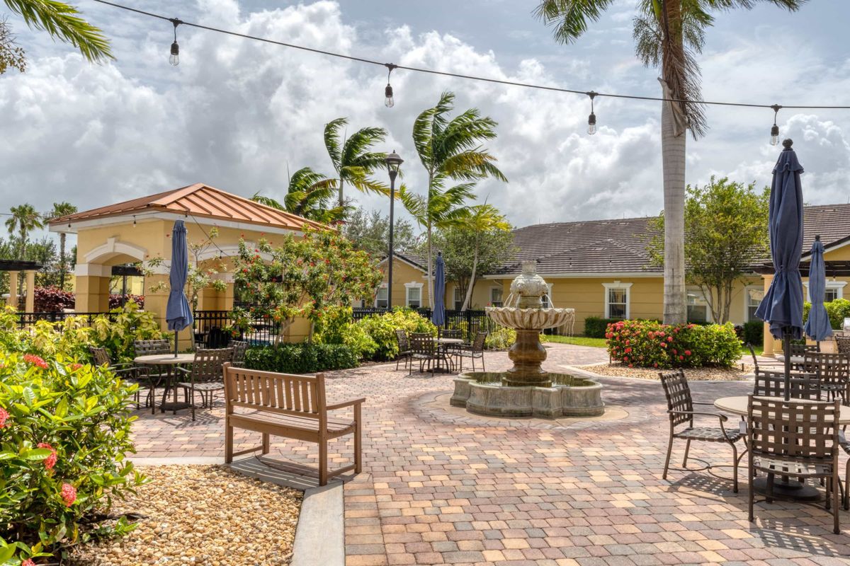 A peaceful courtyard with a central fountain, surrounded by benches and outdoor seating under palm trees.