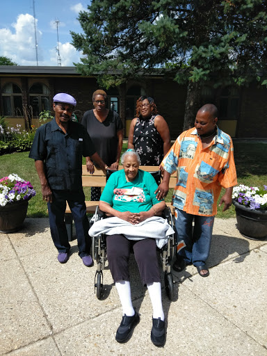 A joyful family gathering with a beloved senior member enjoying a sunny day outdoors.