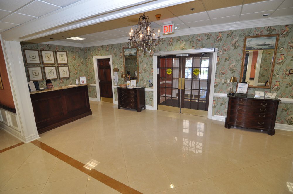 A well-lit lobby with a chandelier, featuring decorative wallpaper and floor tiles, leading to entrance doors.