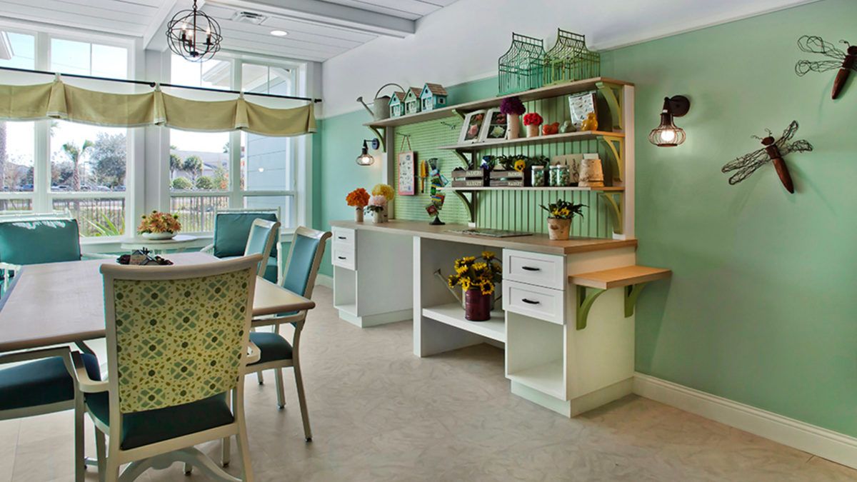 A brightly lit kitchen with green walls, featuring open shelves and white cabinets, alongside a dining area with chairs and a table.