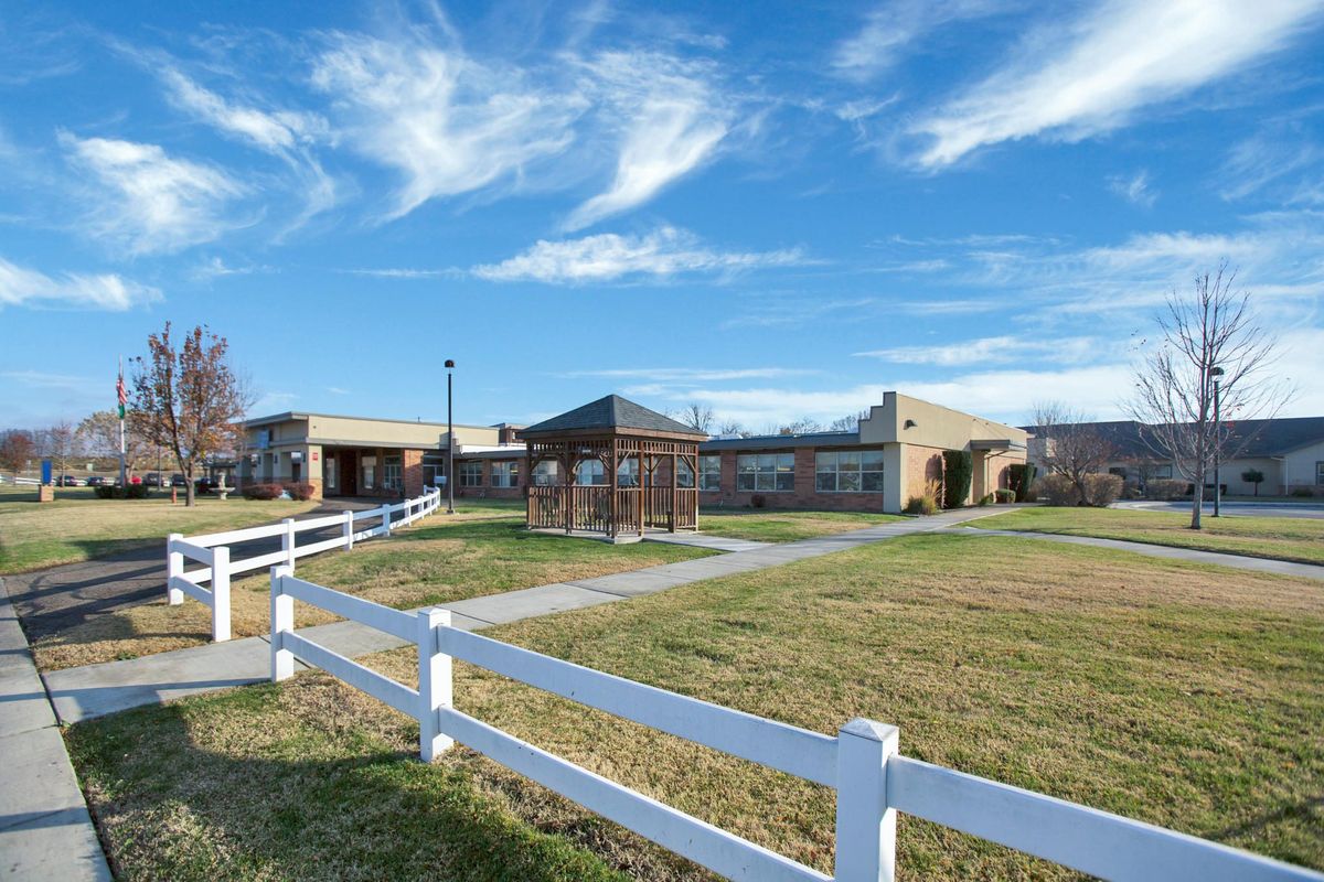 A scenic view of a building with a white fence and open grassy area under a blue sky with clouds.