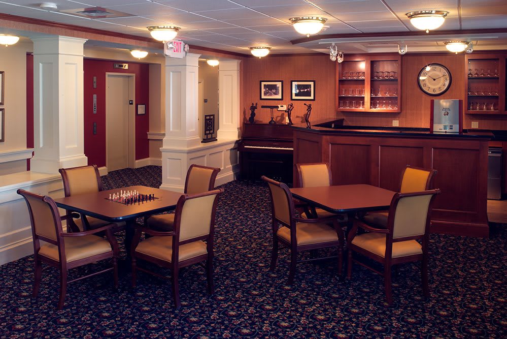 A cozy interior dining space with several tables and chairs, featuring a carpeted floor and a small bar area.