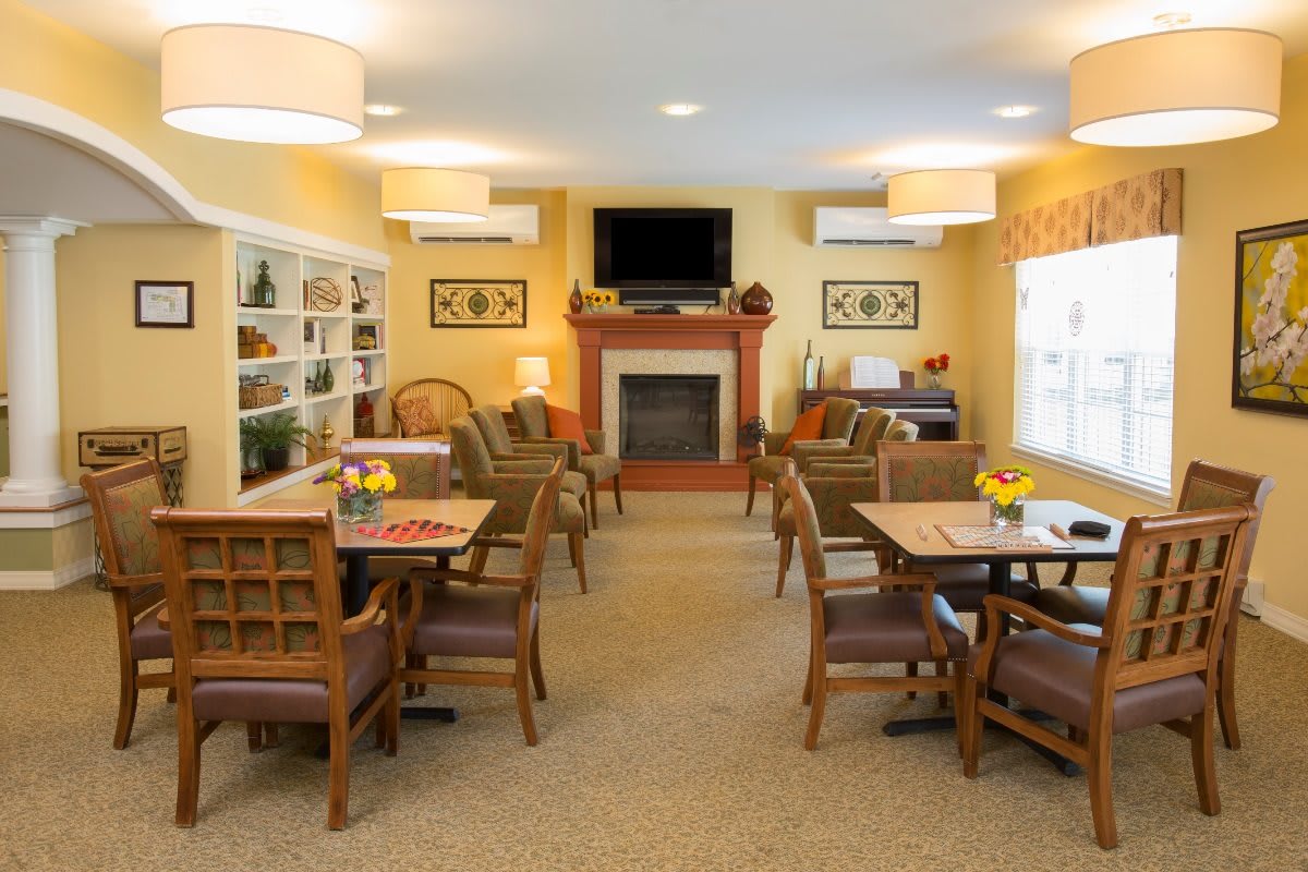 A cozy and well-furnished common living area with tables, chairs, a fireplace, and a television.