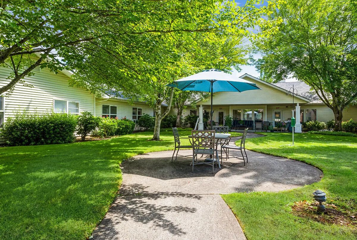 A sunny backyard patio with a table and umbrella set amidst a lush garden.