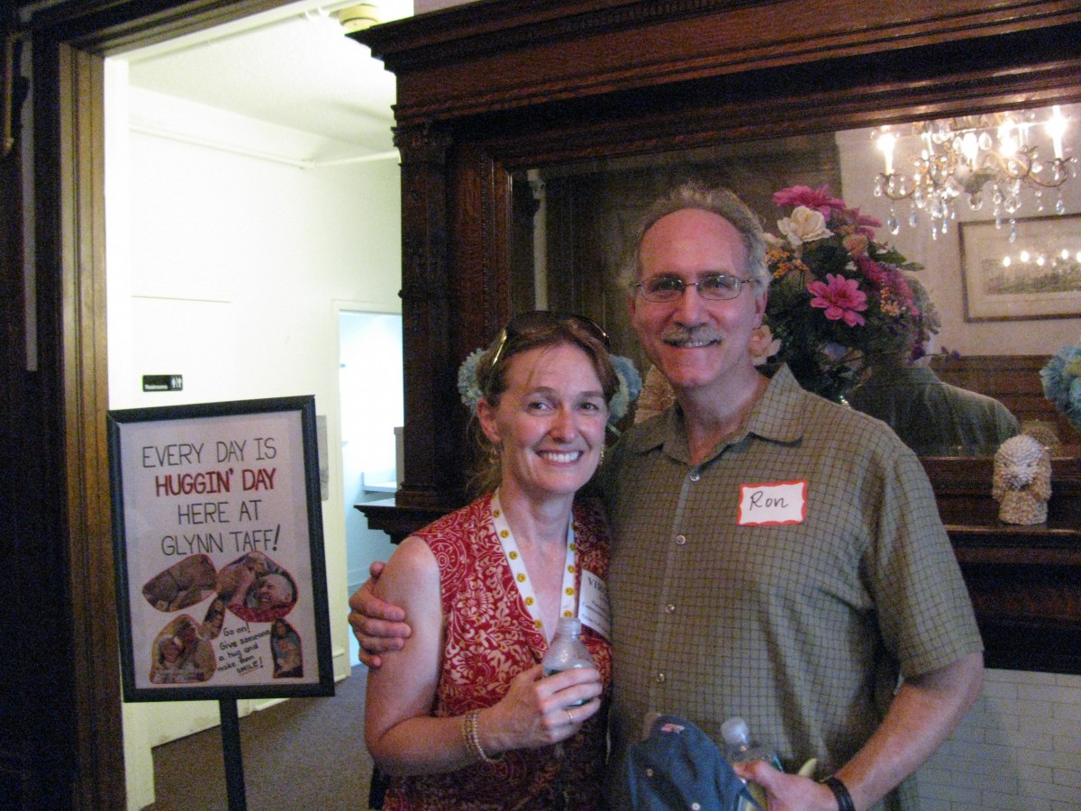 Two people smiling at an indoor event with floral decor and a sign in the background.