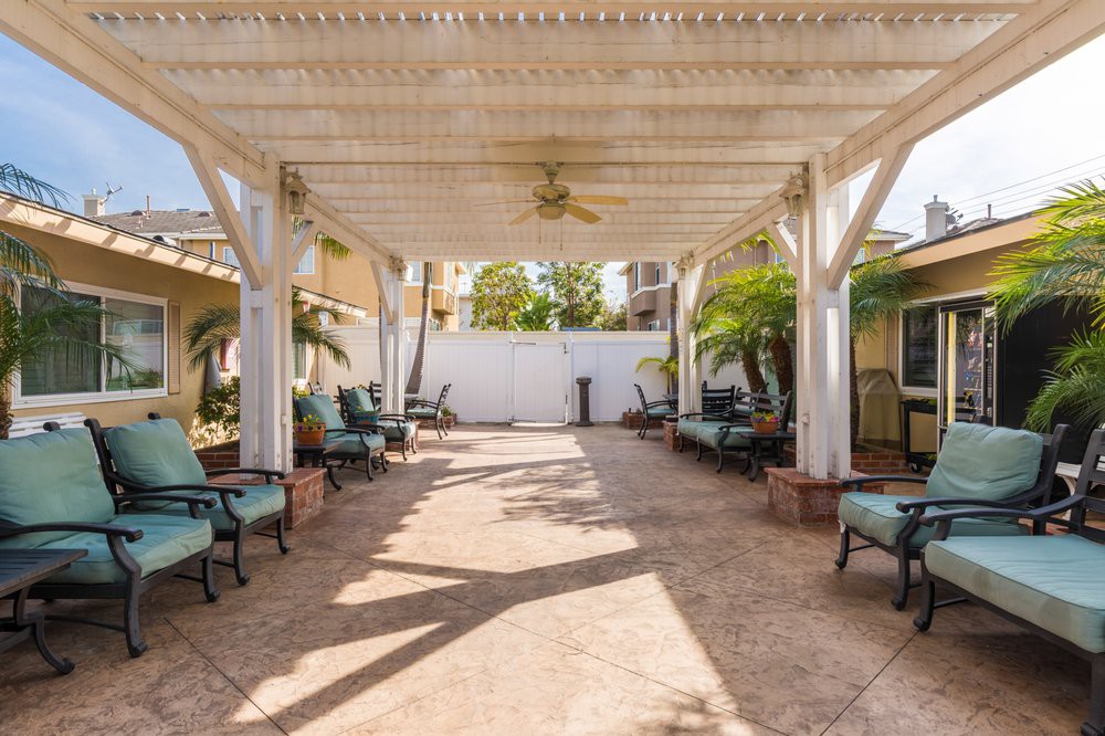 A spacious backyard patio featuring a pergola with outdoor seating and lush palm trees.