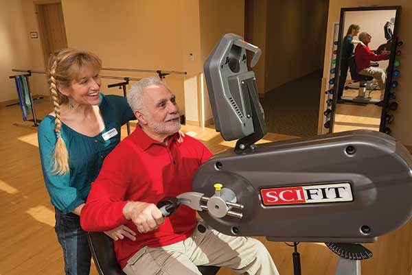 An elderly man using exercise equipment with assistance from a trainer.