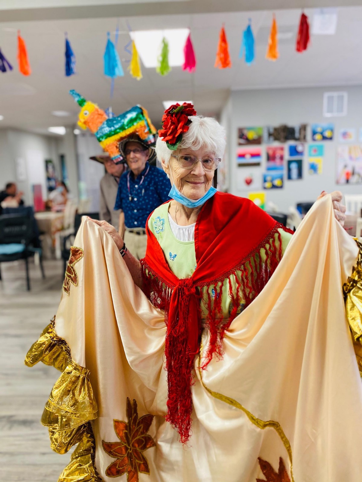 An elderly woman dressed in colorful traditional attire and a festive hat participates in a cultural celebration.