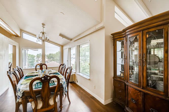 A bright dining room with a wooden table set, chandelier, and large windows.