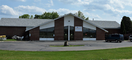 A modern commercial building with a spacious parking area and large windows, surrounded by greenery.