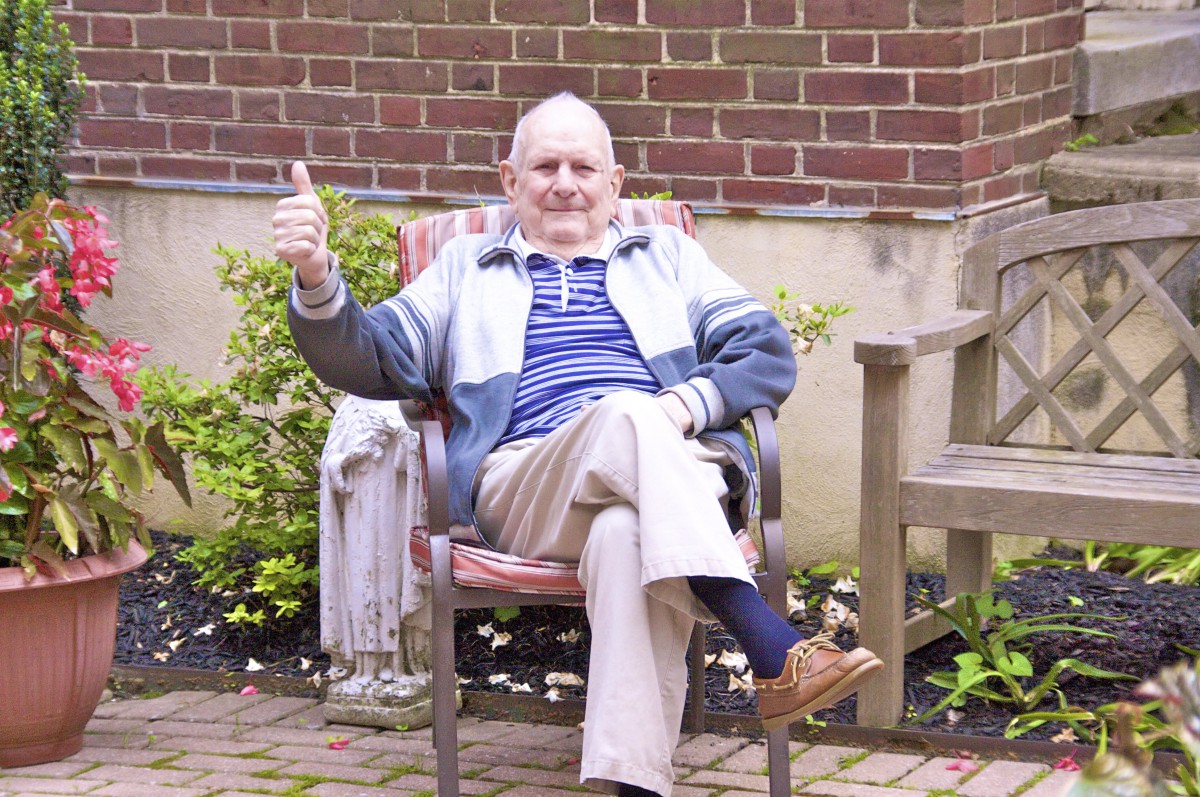 An elderly man sitting comfortably in a garden chair, giving a thumbs up gesture.