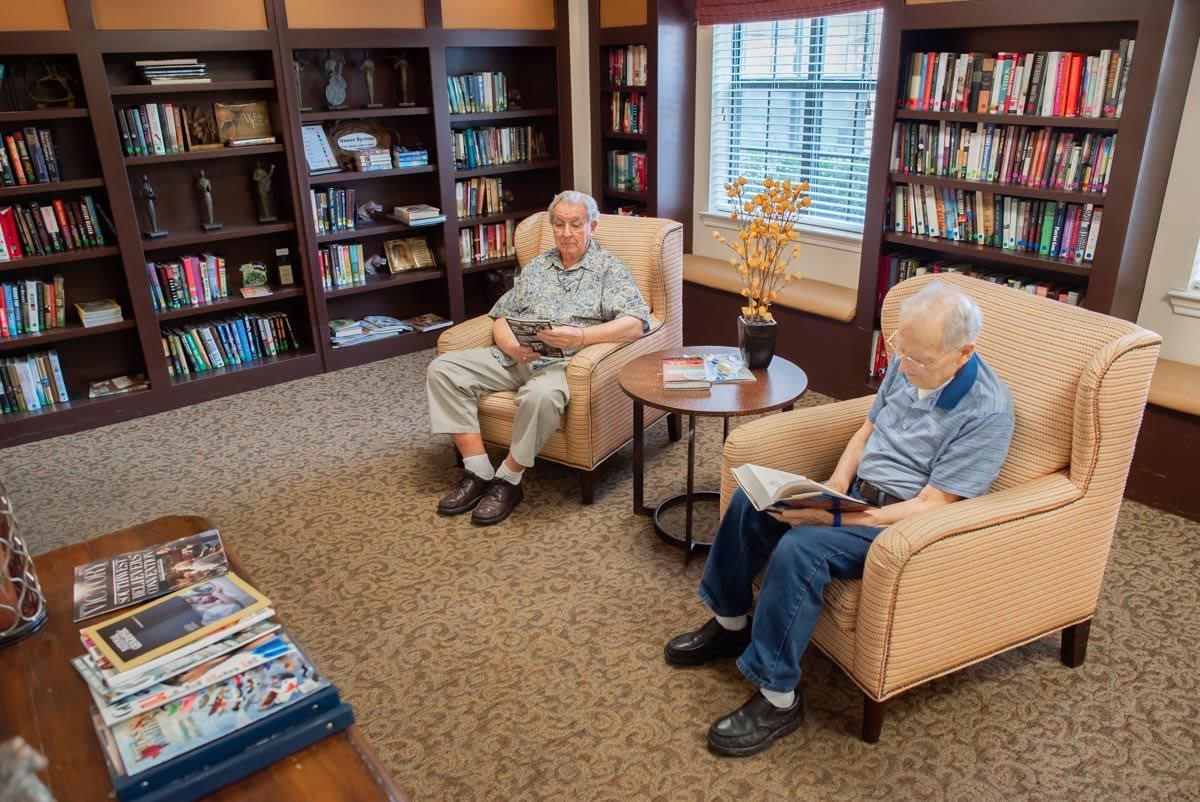 Two seniors reading books in a cozy library setting.