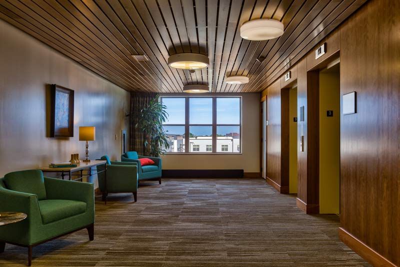 A modern lobby area featuring comfortable seating and elevator access, illuminated by natural light.