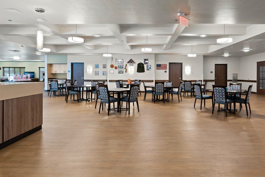 An empty dining area with neatly arranged tables and chairs, featuring wooden flooring and ceiling lights.