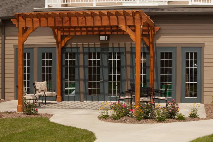 A wooden pergola with outdoor seating on a patio, surrounded by a landscaped garden.