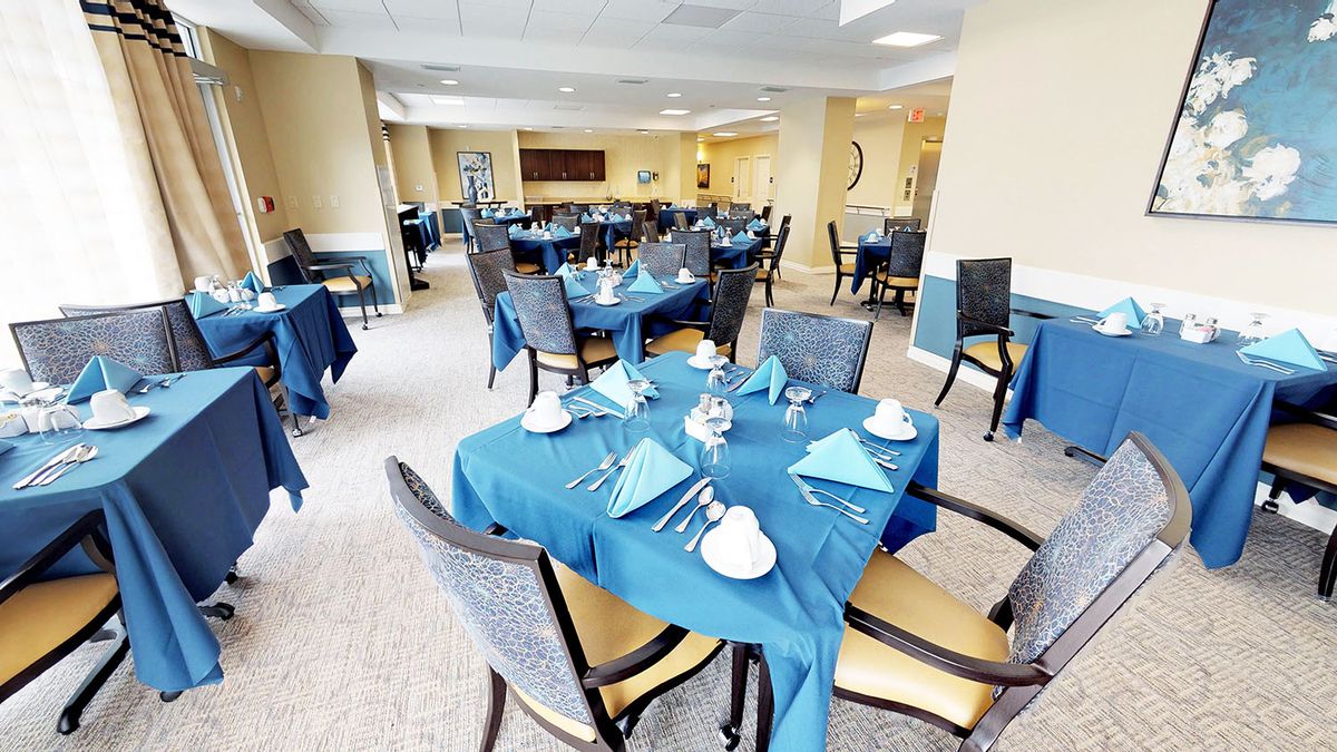 An elegant dining room with tables set for guests, featuring blue tablecloths and neatly arranged place settings.