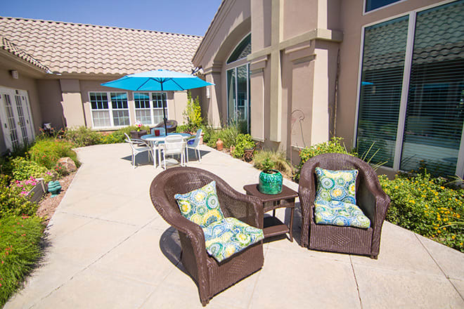 A sunny patio featuring wicker chairs with patterned cushions and a table with an umbrella.