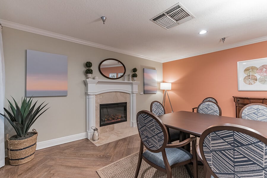 A cozy living room featuring a fireplace, dining table with chairs, and wall art.