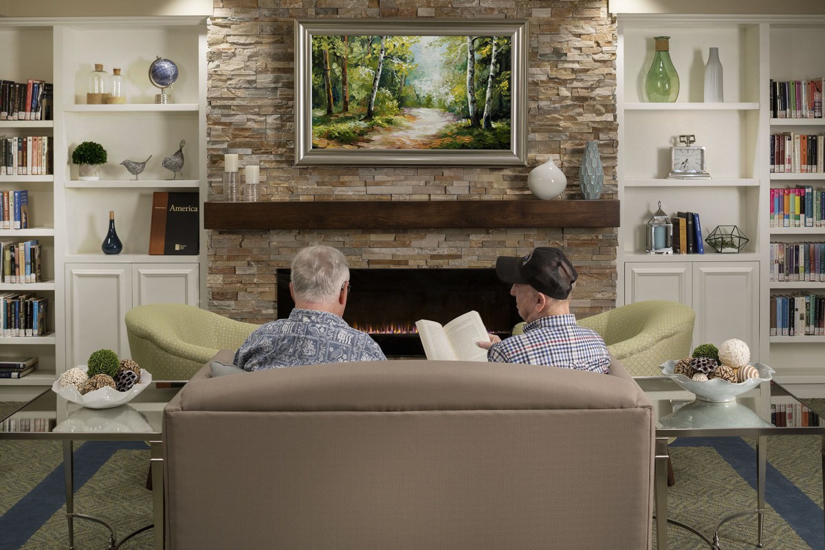 Two people sitting on a couch in a cozy living room with a fireplace and artwork.