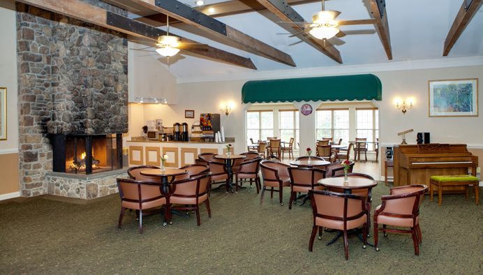 A cozy dining area with wooden beams, a stone fireplace, and neatly arranged tables and chairs.