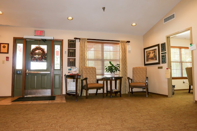 A cozy lobby area with chairs and a small table, adorned with paintings and a window overlooking outside.