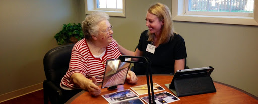 A heartwarming moment between a caregiver and an elderly woman, sharing memories through photos.