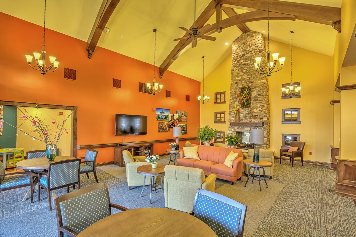 A cozy living room with an orange accent wall, high ceilings with wooden beams, a stone fireplace, and comfortable seating.