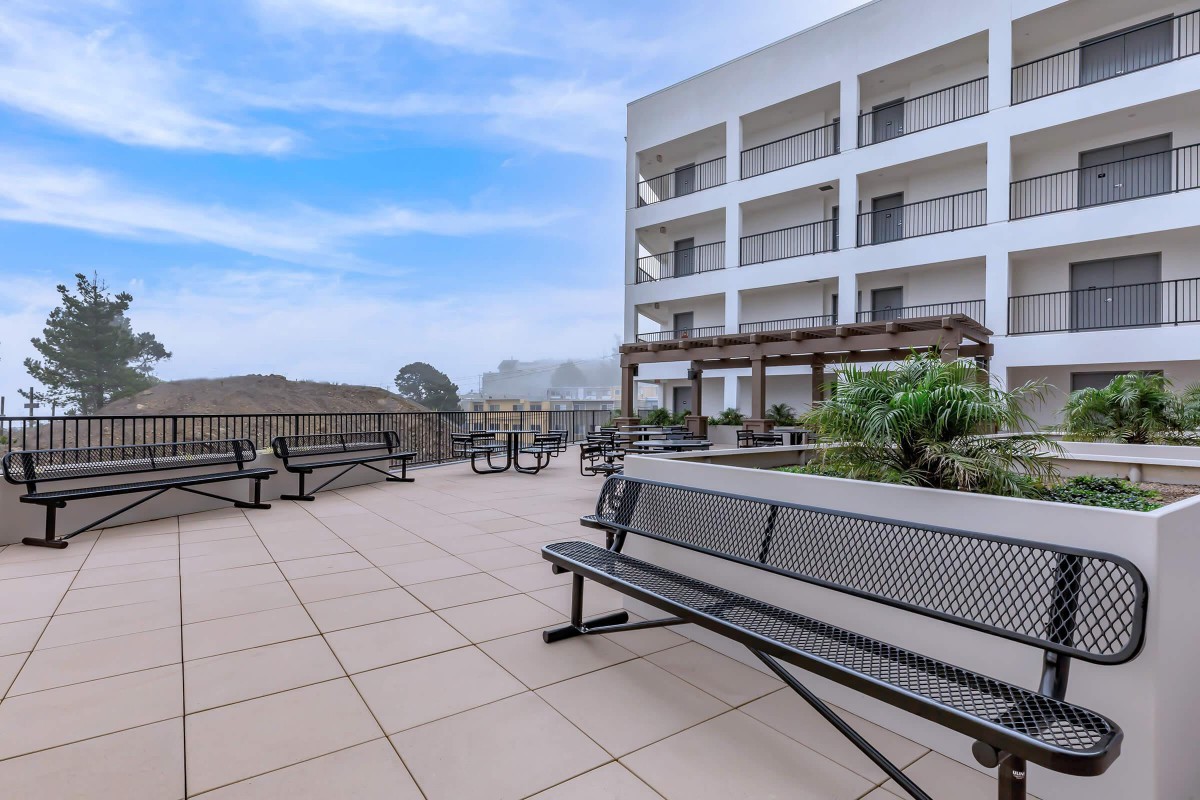 A spacious outdoor patio area with benches and a view of a modern building under a clear blue sky.