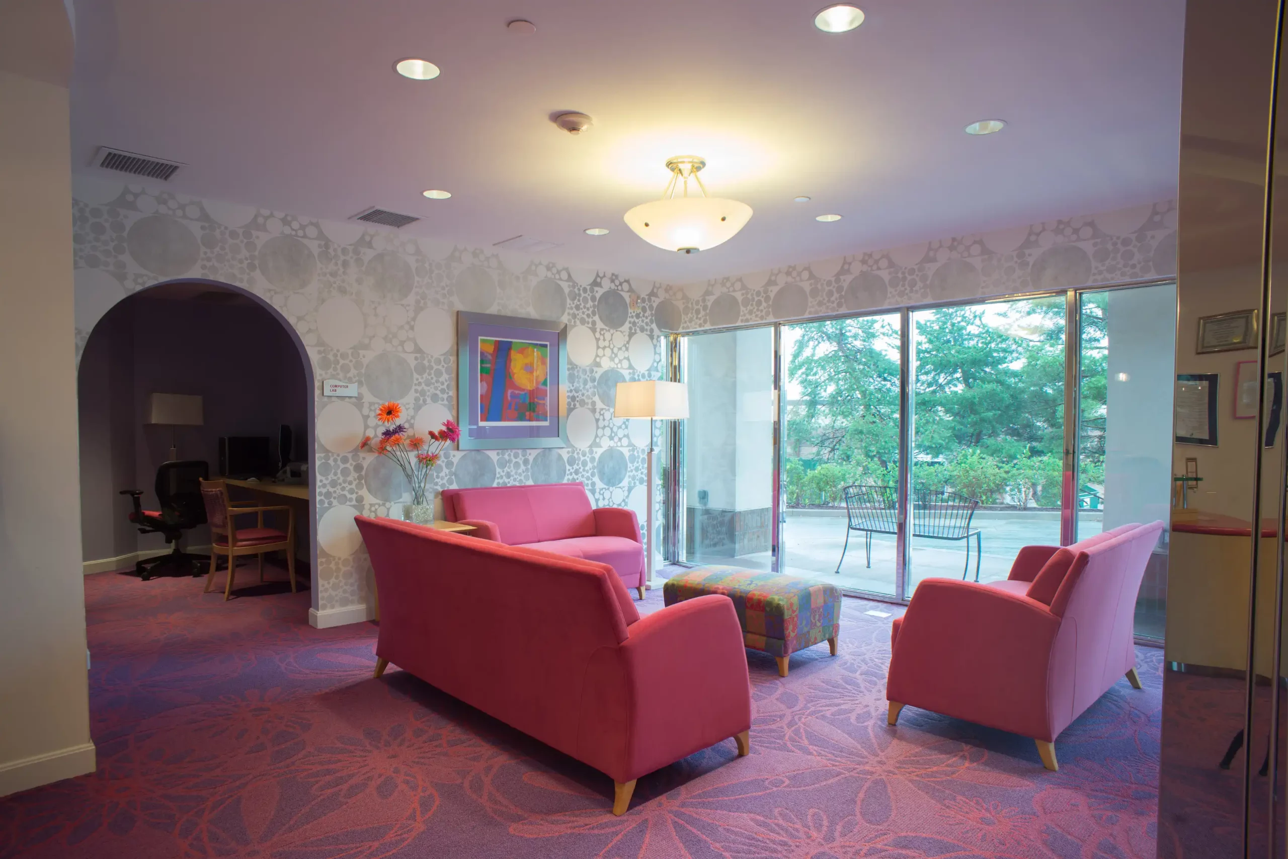 A cozy living room with red sofas and chairs, featuring a large window and modern lighting.