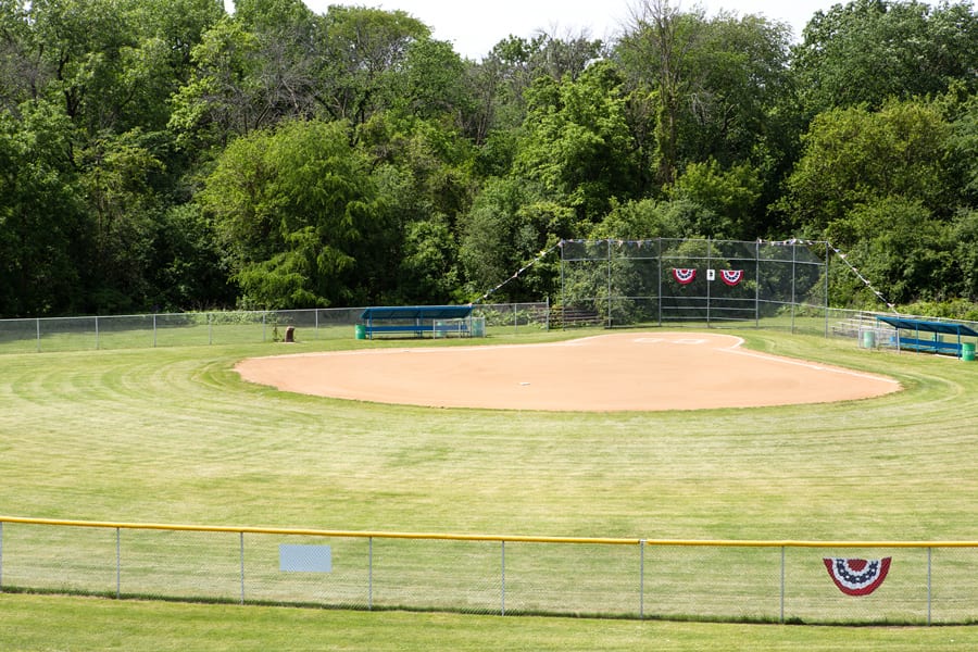 A baseball field surrounded by trees and a fence, with a bench in the background.