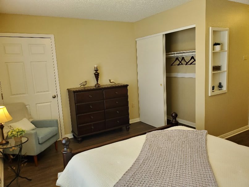 A cozy bedroom featuring a dresser, an open closet, and a comfortable chair in neutral tones.