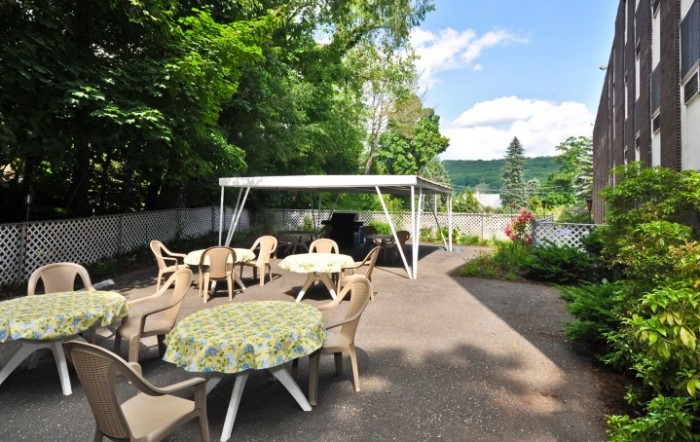 A sunny outdoor patio with tables, chairs, and a gazebo surrounded by greenery.