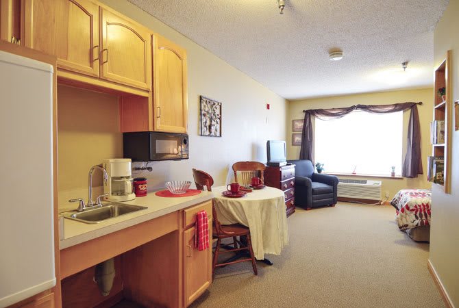 A cozy studio apartment with a compact kitchen area and a small dining table set next to a window.