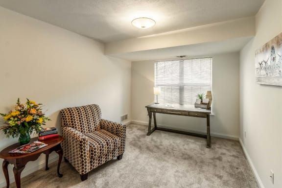 A cozy room with a patterned chair, desk, and window.