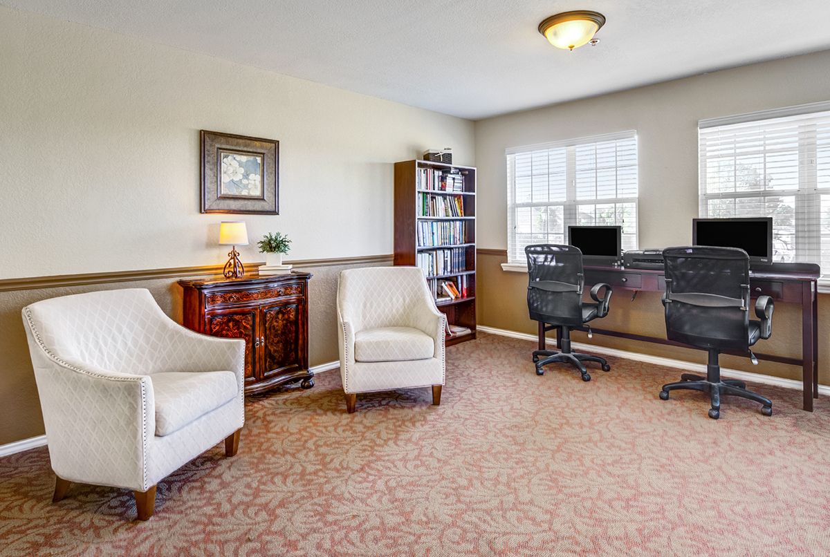 A well-lit office space featuring two comfortable chairs, a desk with a computer, and a bookshelf by the window.
