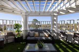 A stylish outdoor seating area under a pergola with sofas and potted plants, bathed in sunlight.