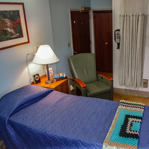 A cozy bedroom featuring a bed with blue bedding, a green chair, a bedside lamp, and decorative elements.