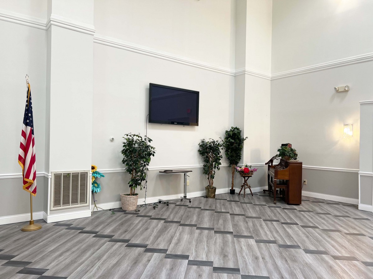 A modern living space featuring a wall-mounted television, several potted plants, and a piano in the corner.