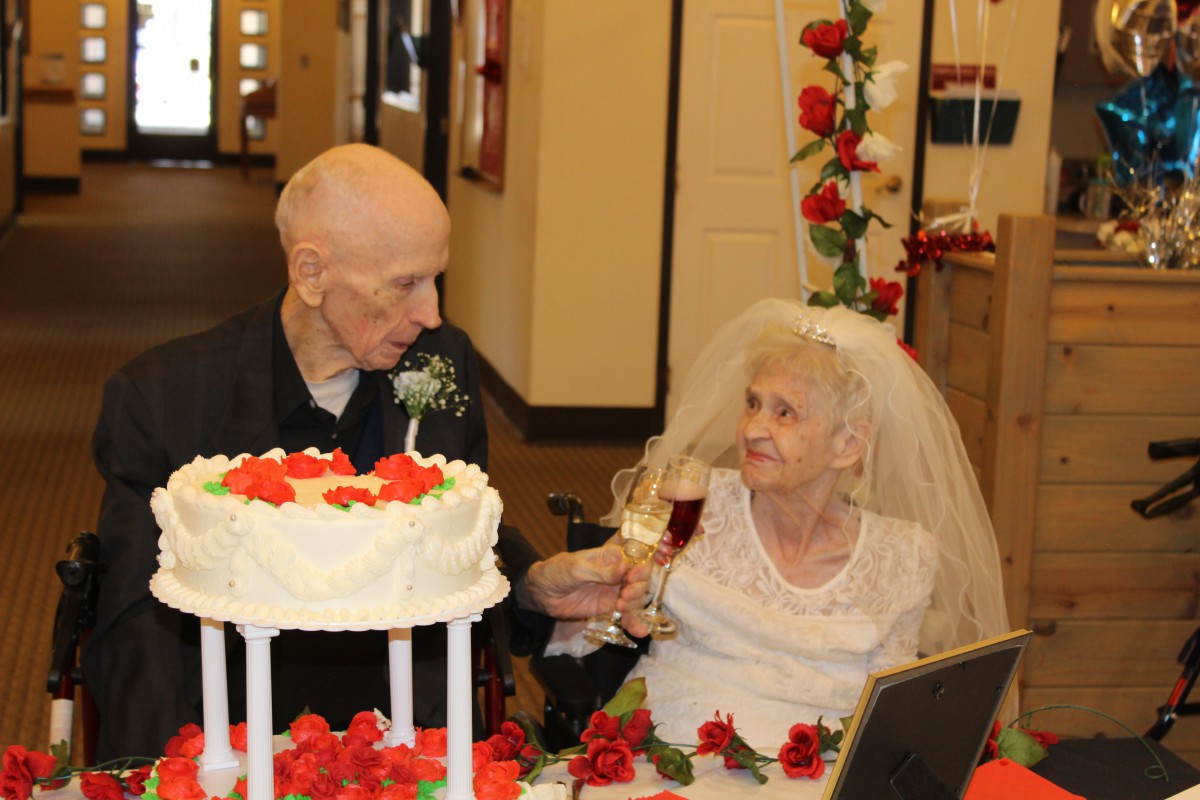 An elderly couple celebrates their wedding with a cake and a champagne toast.