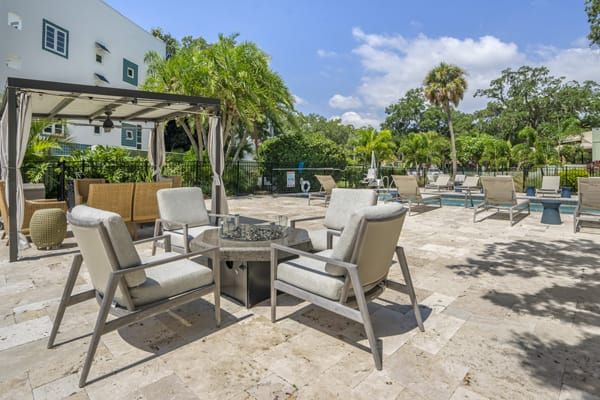 A sunny patio area with comfortable seating and a table, surrounded by lush greenery.